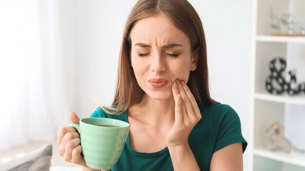 A woman experiencing tooth pain while holding a cup of tea, possibly indicating a need for oral surgery in Plymouth, MI