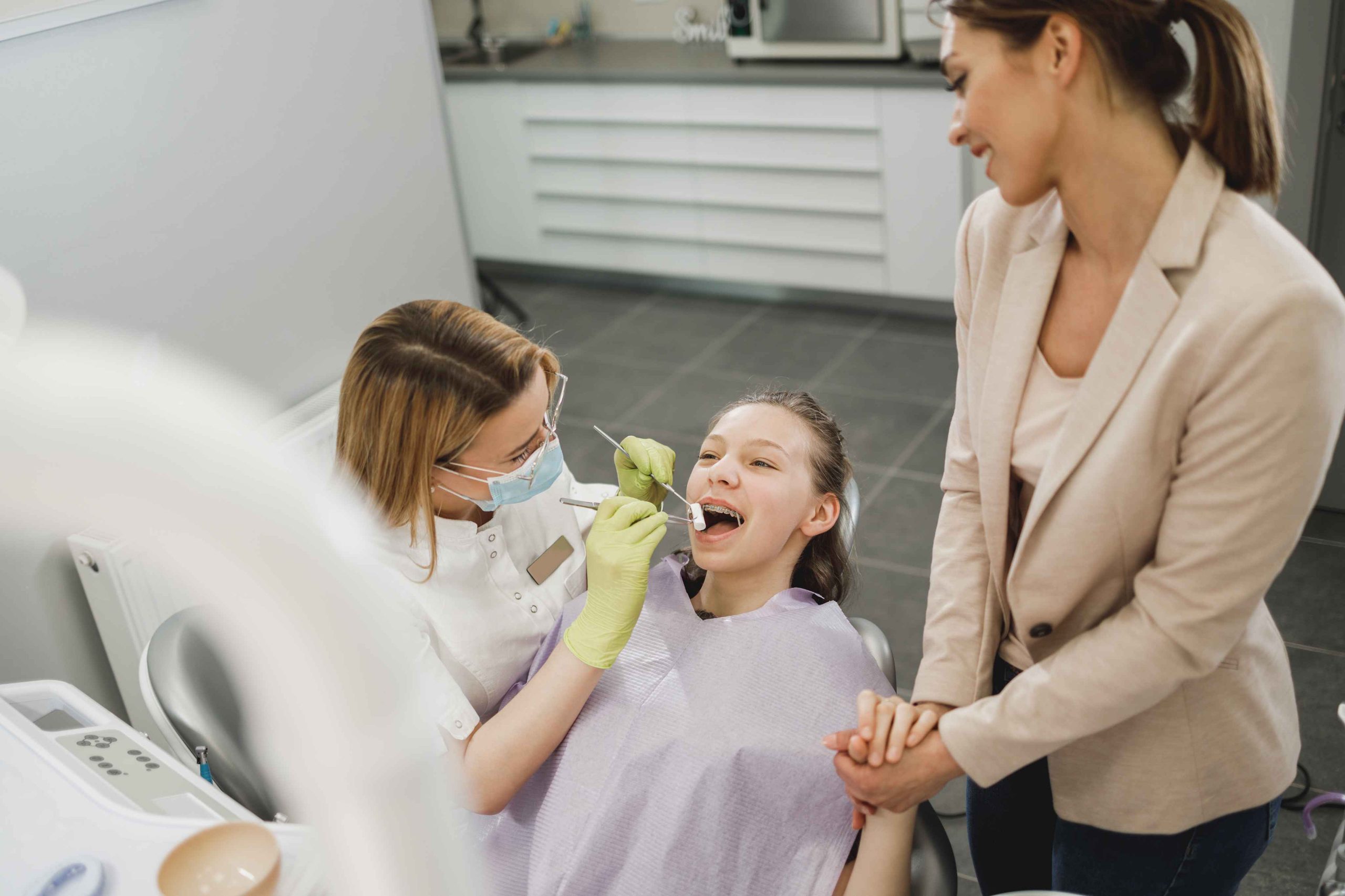 Child receiving a dental exam with her mother nearby.